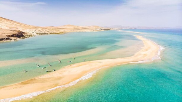 Vista aérea de una playa con aguas turquesas cristalinas y una orilla arenosa.