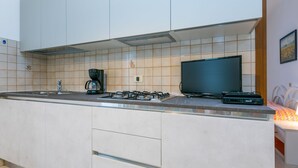 A modern kitchen with a gas stove, coffee maker, and a flat-screen TV.