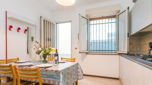 A dining area with a table set for two, wooden chairs, a vase with flowers, and a window with bars.