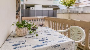 An outdoor balcony with a table set for two, featuring a tablecloth with a fish pattern, a wicker basket, and a glass of red wine.