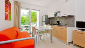 Una cocina moderna con armarios blancos, un microondas y una estufa a gas. Hay un comedor con una mesa y sillas blancas, y un sofá naranja brillante.