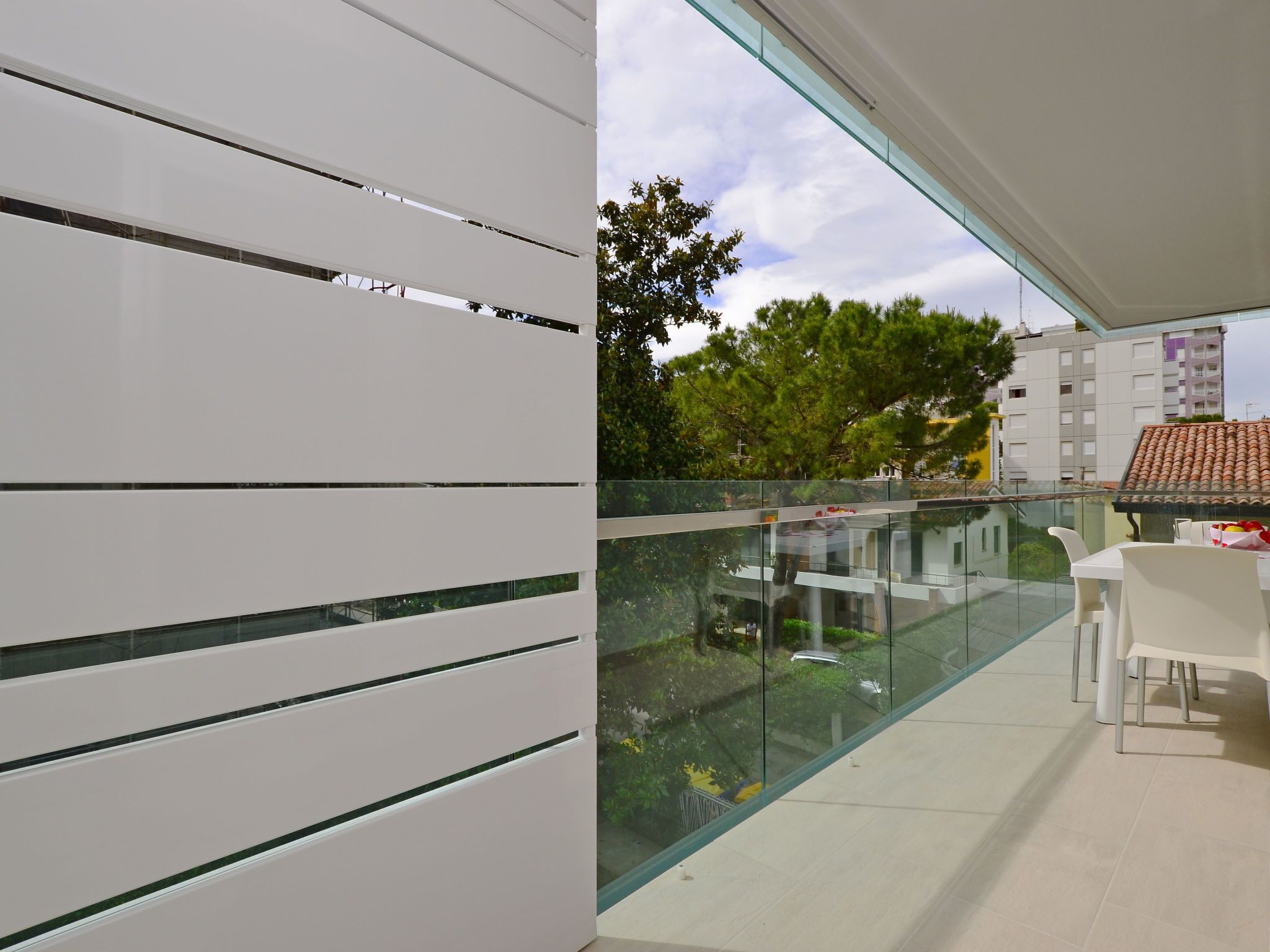 A balcony with a glass railing, a white chair, and a table.