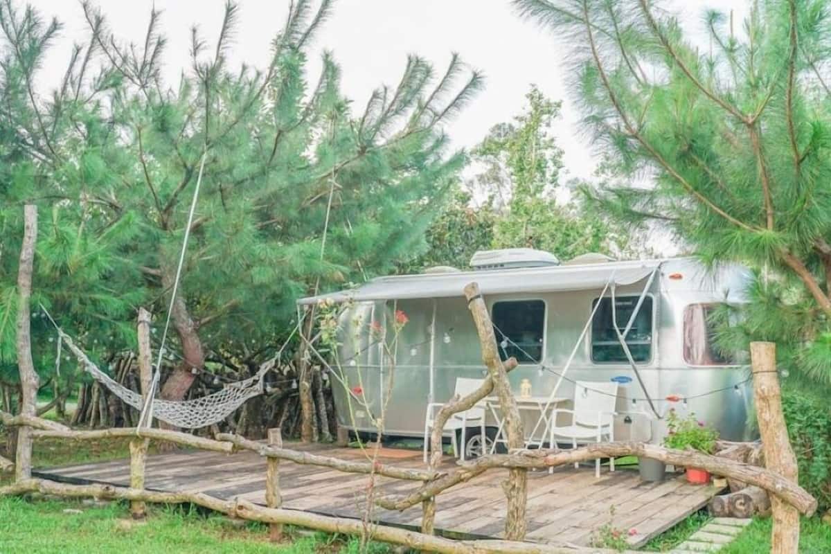 A recreational vehicle (RV) parked in a wooded area with a hammock and a small table and chair set up nearby.