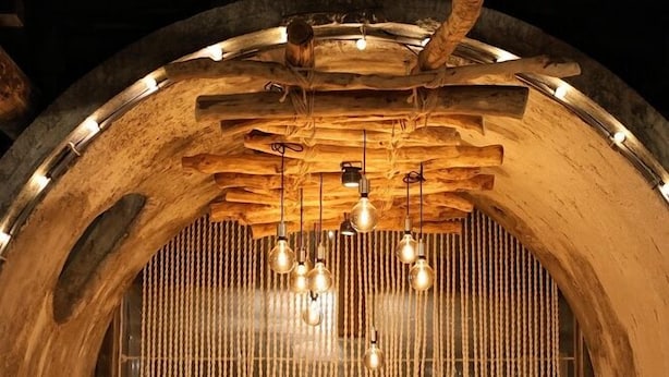 A rustic interior with a wooden barrel structure, hanging light fixtures, and a woven curtain. - OrangeFarmerlife (Zhuolan)