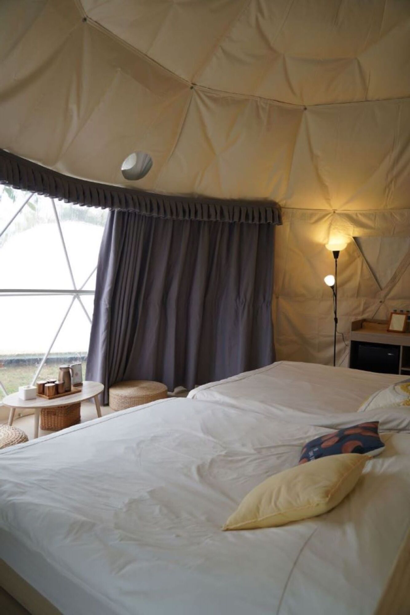 A spacious tent with a bed, a table, and a lamp.