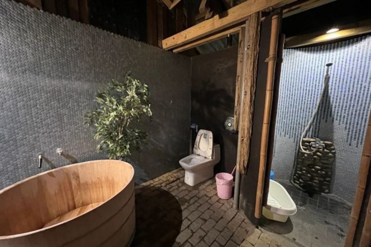 Une salle de bain rustique avec une baignoire en bois, des toilettes et une petite plante.