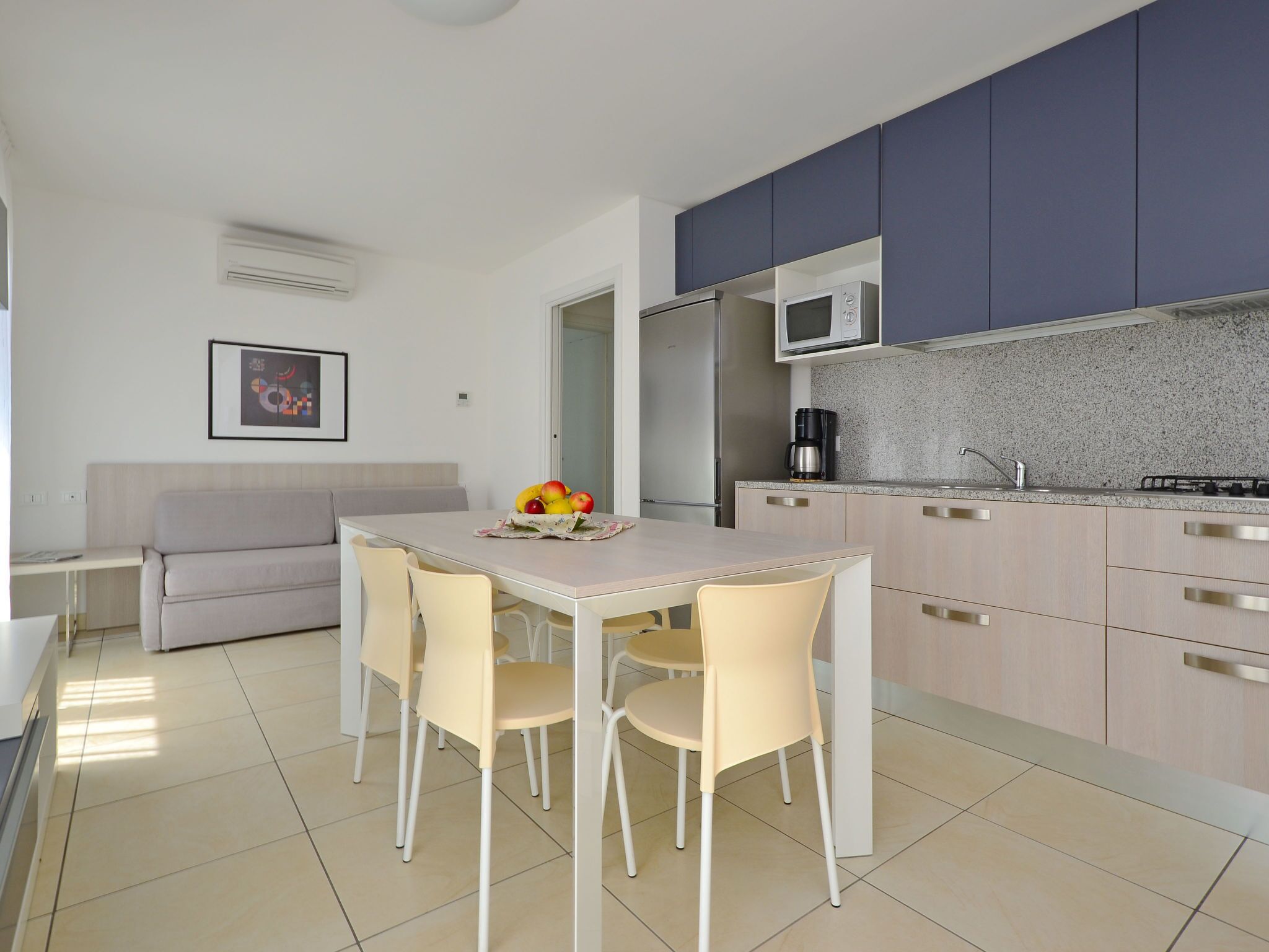 Una cocina moderna con comedor, que incluye una mesa con sillas, microondas, refrigerador y cafetera.