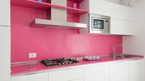 A kitchen with pink walls, white cabinets, a stainless steel microwave, a gas stove, and a sink.