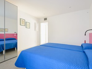 Habitación de hotel con dos camas, un espejo grande y una puerta que da a otra habitación.