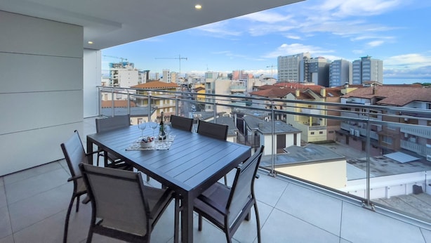 Un balcón con mesa y sillas, con vistas a un paisaje urbano con edificios y grúas de construcción.