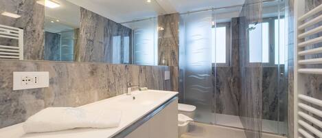 Un baño moderno con tocador de mármol, cabina de ducha de vidrio y un espejo grande.