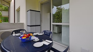 Una mesa redonda dispuesta para dos, con mantel azul, platos blancos, cubiertos y una cesta de frutas.