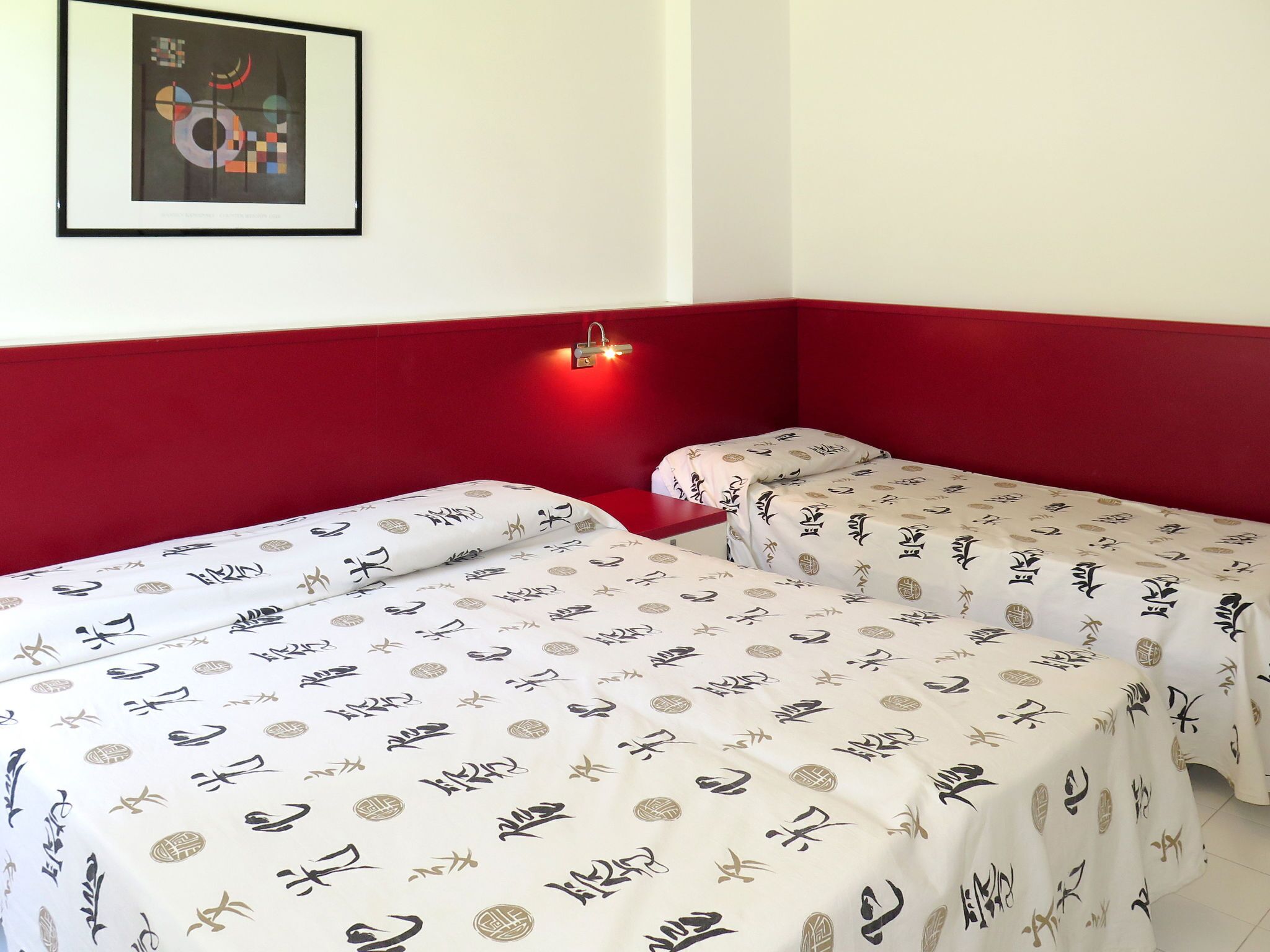 Ein Zimmer mit zwei Betten, jedes mit einer weißen Bettdecke mit chinesischen Schriftzeichen. Darüber an der Wand hängt ein gerahmtes abstraktes Gemälde.
