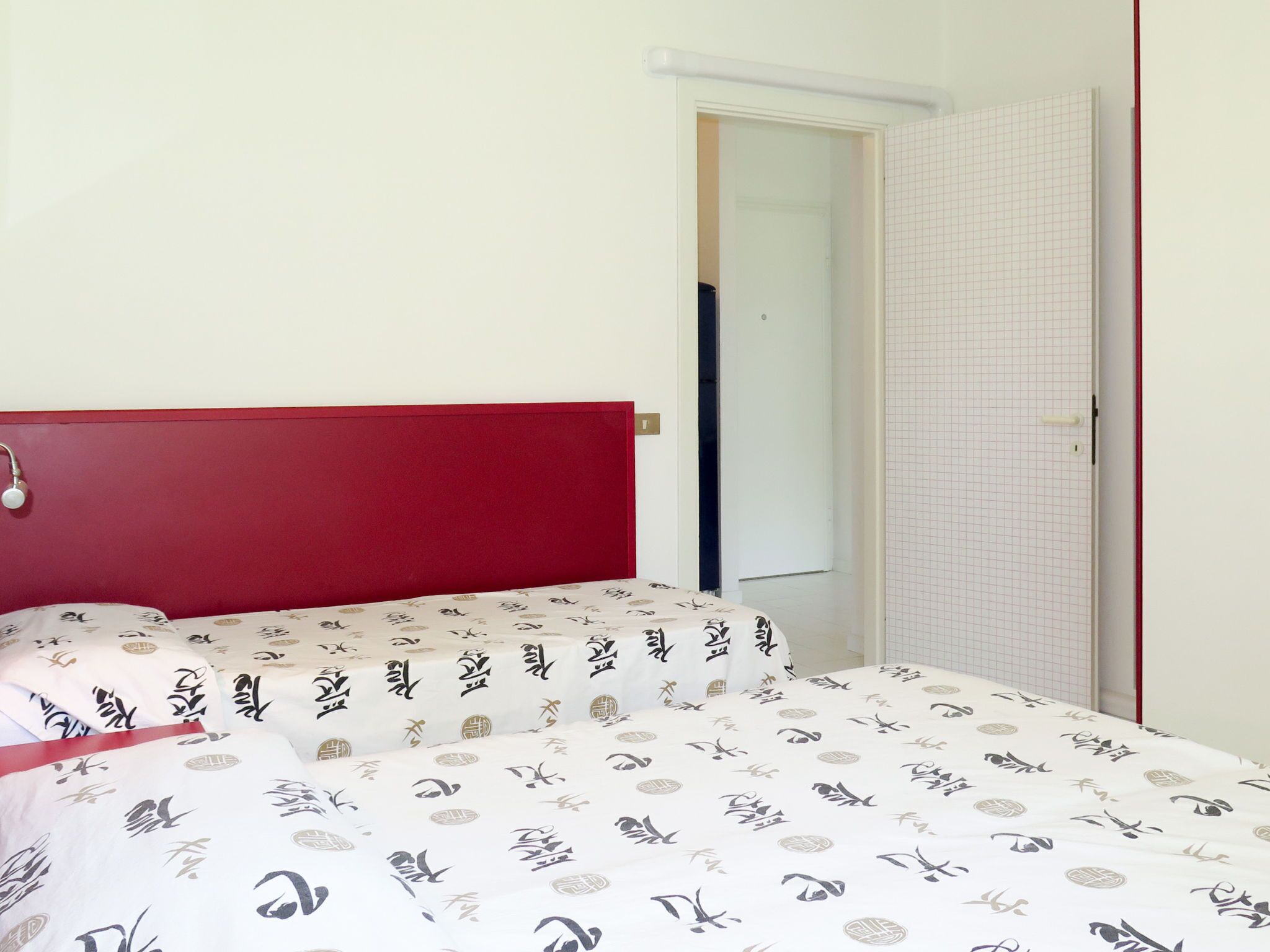 Un dormitorio con cabecera roja, cama con colcha estampada y puerta con diseño de cuadrícula.