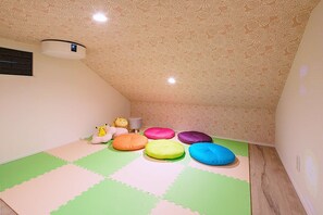 Une pièce avec un plafond en pente, un climatiseur fixé au mur et des poufs colorés disposés sur un sol vert et blanc composé de dalles modulaires.