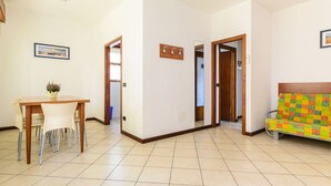 Een ruime woonkamer met een eethoek, een bank en een keuken, zichtbaar door een open deur.