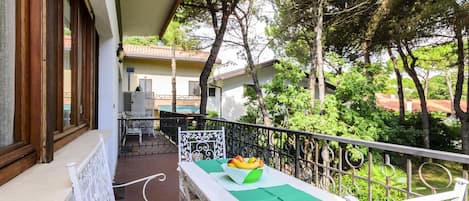 A balcony with a table and chairs, surrounded by trees and a building in the background.
