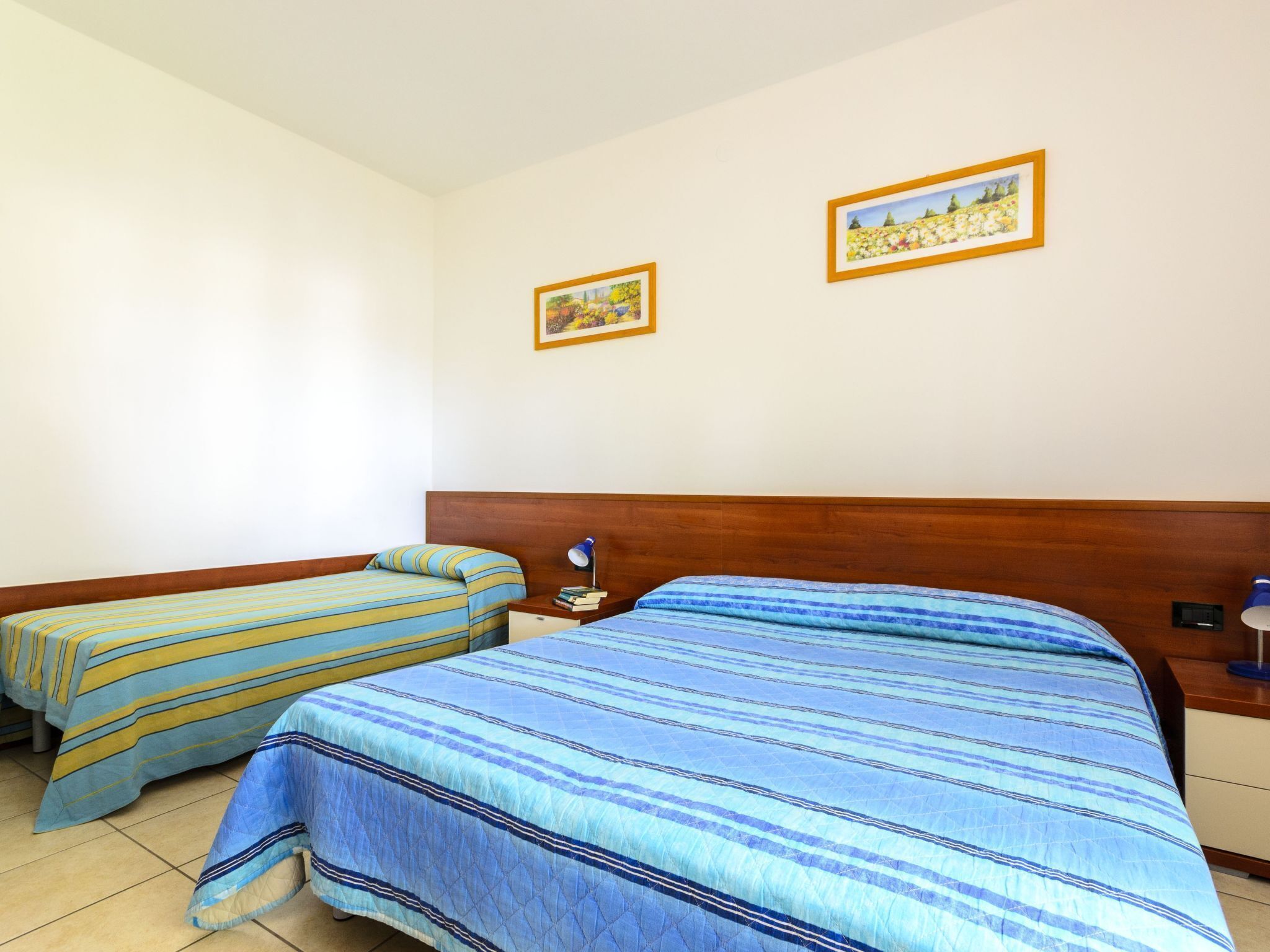 Ett hotellrum med två sängar, en sänggavel i trä och två inramade tavlor på väggen.