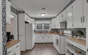 A compact kitchen with white cabinets, a stove, and a refrigerator.