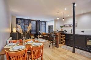 A modern kitchen with a central island, dining area with wooden chairs, and a living space with a sofa and coffee table. - Apartment in the Center of Paris by Studioprestige (Paris)