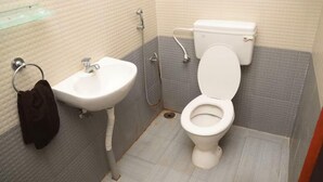 Uma casa de banho pequena com uma sanita, chuveiro e lavatório brancos.