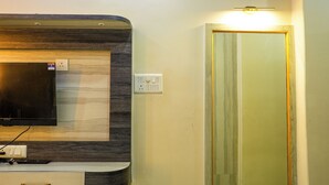 A modern bathroom with a built-in vanity, a flat-screen TV, and a mirror with a wooden frame. - Sun High Stay Luxury Guest House (Varanasi)