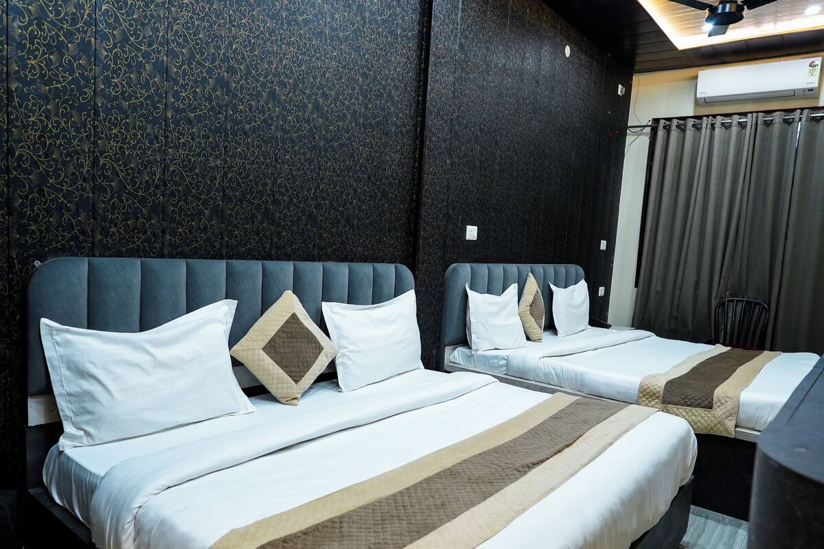Hotellihuone, jossa on kaksi sänkyä, tumma kuvioitu tapetti ja kattotuuletin.