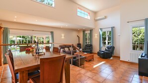 A spacious living area with a wooden dining table, comfortable seating, and large windows offering views of greenery. - Mozamb - Javea, Costa Blanca (Javea)