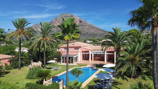 A resort with a swimming pool, palm trees, and a mountain in the background. - Mozamb - Javea, Costa Blanca (Javea)