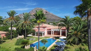 A resort with a swimming pool, palm trees, and a mountain in the background. - Mozamb - Javea, Costa Blanca (Javea)