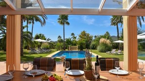 A dining area with a pool view, featuring a table set for four with wine glasses, plates, and a fruit bowl. - Mozamb - Javea, Costa Blanca (Javea)
