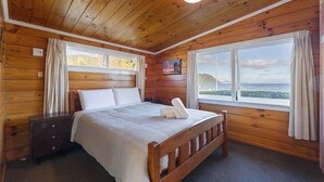 A wooden cabin bedroom with a bed, nightstands, and a window with a view of the sea. - 3 Oaks on the Lake -  Kinloch (Kinloch)