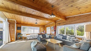 A cozy cabin interior with a wooden ceiling, a sofa set, a dining table, and large windows offering a view of greenery outside. - 3 Oaks on the Lake -  Kinloch (Kinloch)