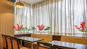 Ein Restaurant mit Holztischen und -stühlen, einer Bank und Kübelpflanzen mit roten Blüten.