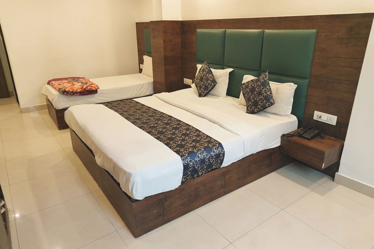A double bed with a wooden frame and a green upholstered headboard. There is a bedside table with a phone and a power outlet.
