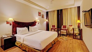 Ein Hotelzimmer mit einem großen Bett, zwei Sesseln, einem Schreibtisch, einem Telefon und einem Fernseher.