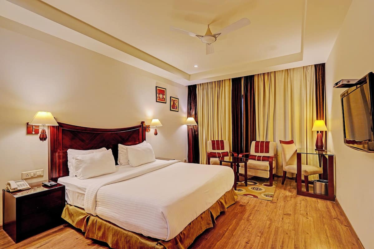 A hotel room with a large bed, two chairs, a desk, a telephone, and a television.
