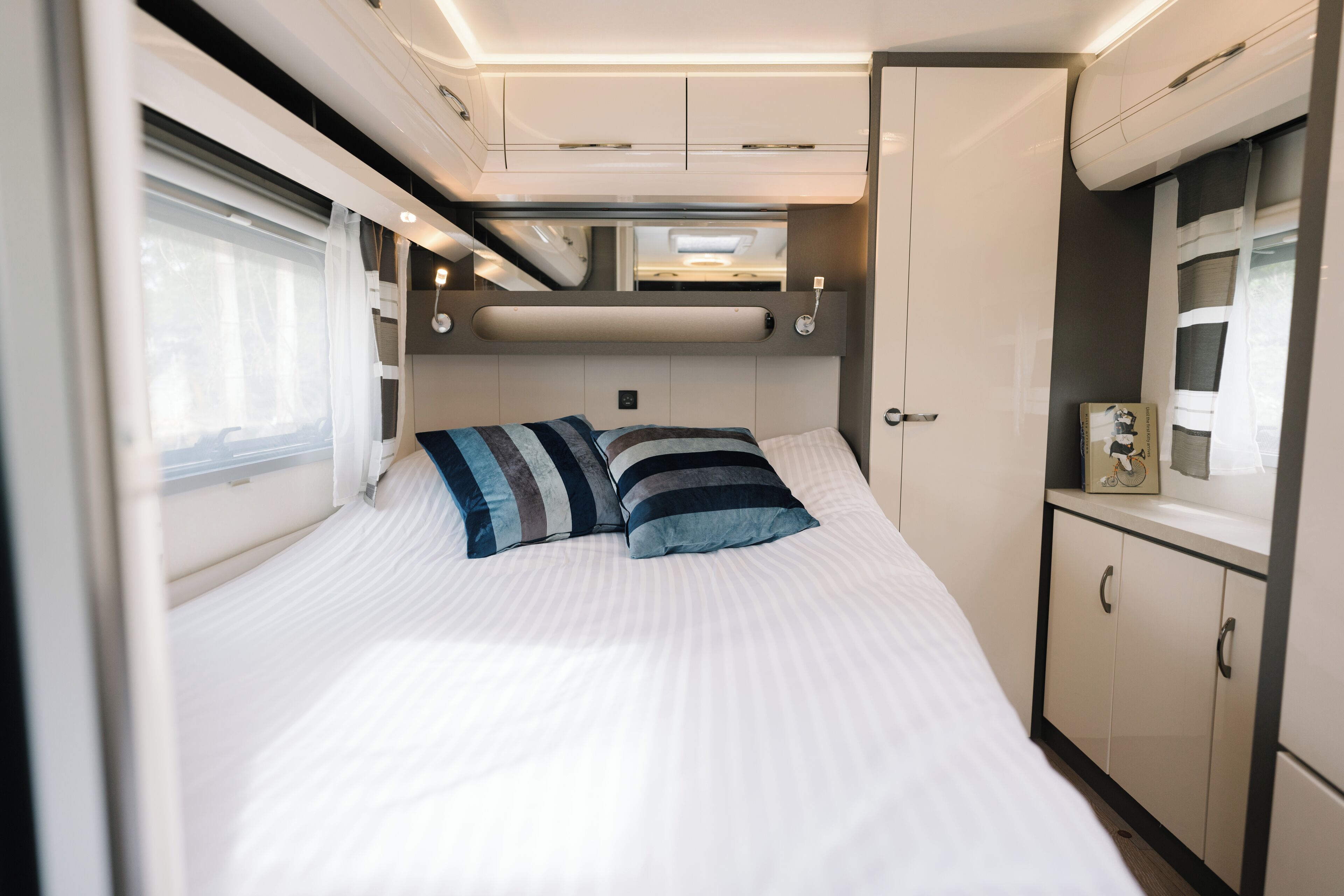 A neatly made bed with striped pillows, a bedside table with a clock, and a wardrobe with a mirror.