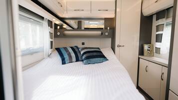 A neatly made bed with striped pillows, a bedside table with a clock, and a wardrobe with a mirror.