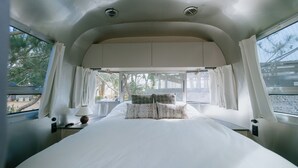 A bed with white bedding and patterned pillows, a bedside lamp, and a window with curtains. - Le.Alley Autocamp Resort (Zhuolan)