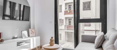 Un salon moderne avec un canapé, deux petites tables et un téléviseur fixé au mur.