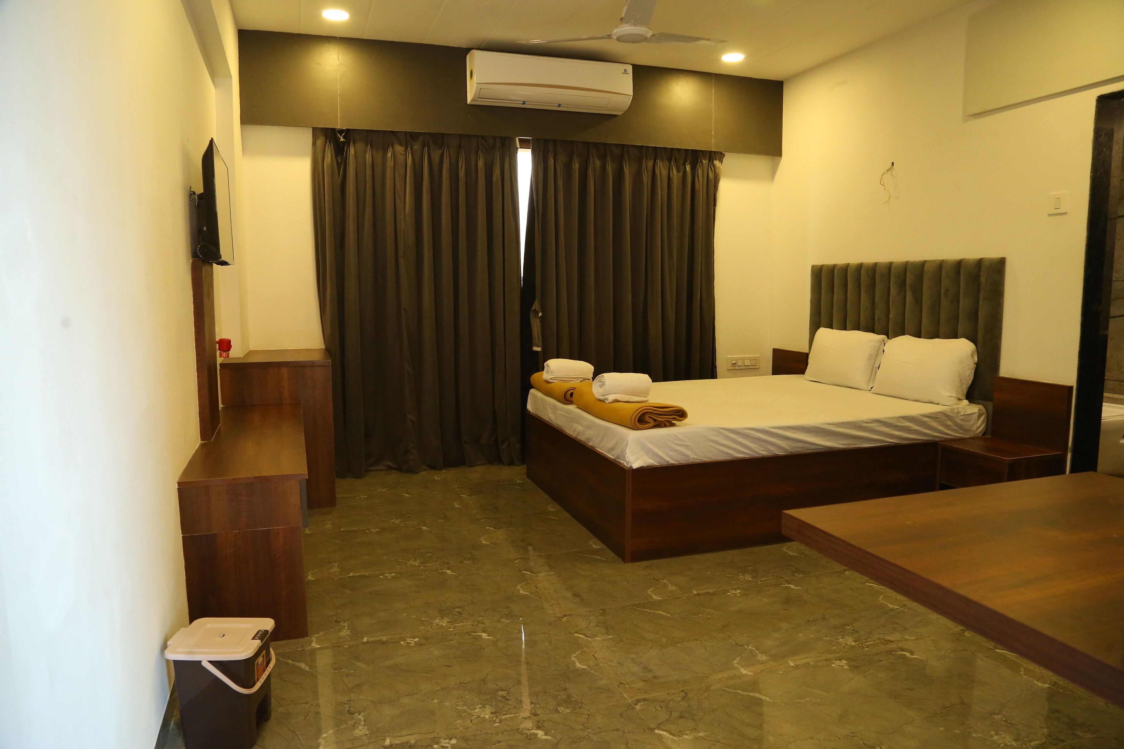 Un dormitorio moderno con cama, un banco de madera, una mesita, teléfono y televisor de pared.