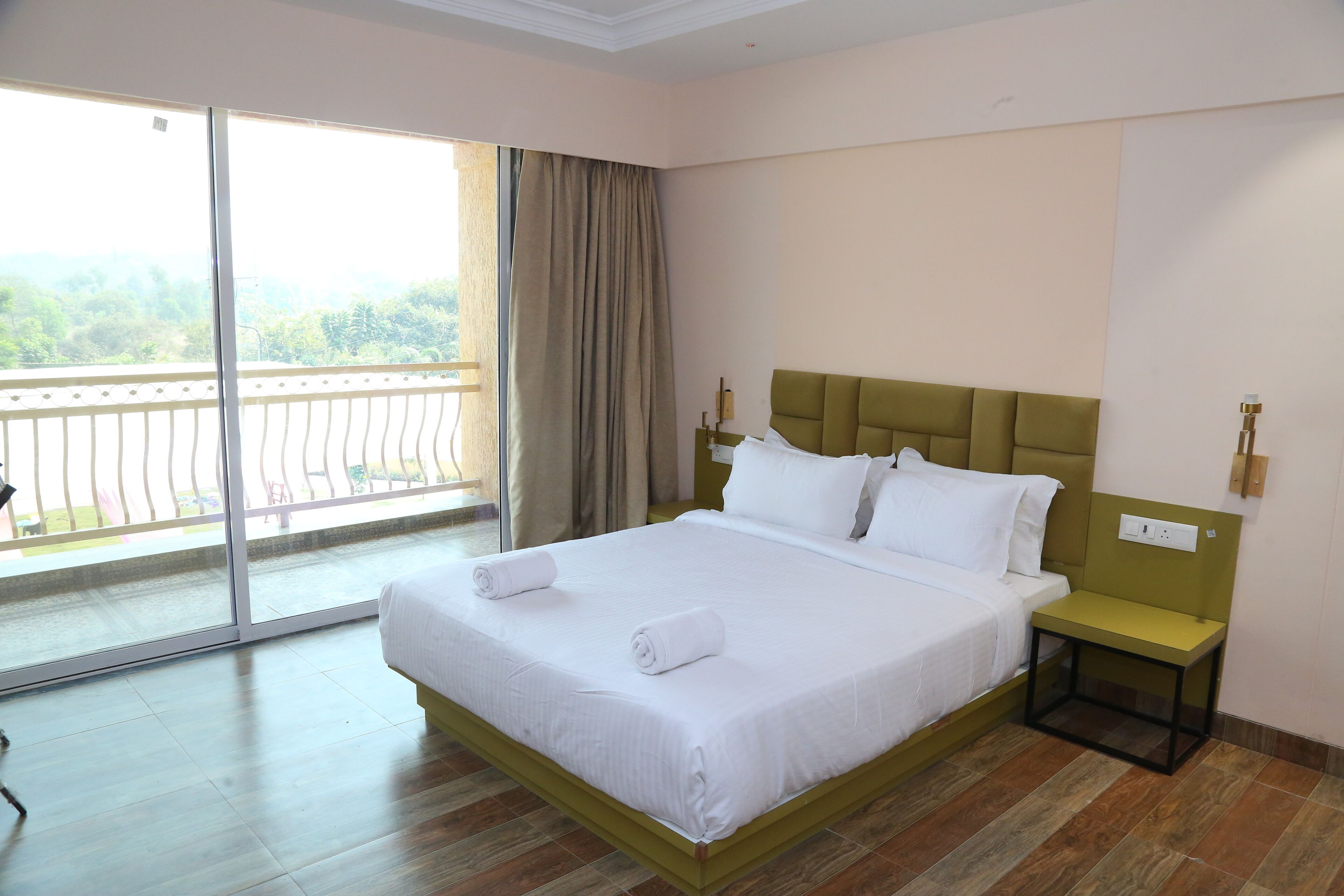 Habitación de hotel con una cama grande, una mesita de noche, un ventanal con vistas a la vegetación y un balcón.