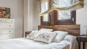 A bedroom with a wooden headboard, a bed with floral bedding, a white dresser, and a window with curtains. - Finca Montechico, Casa Matute, rural Segovia (Segovia)