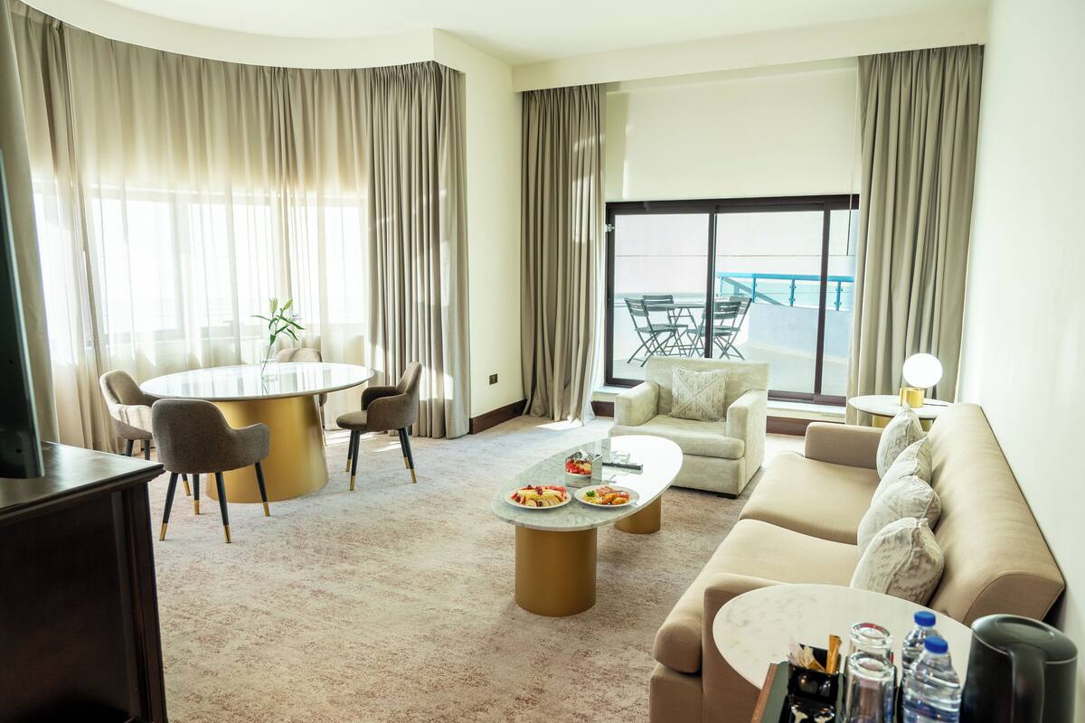 Een moderne hotelkamer met een ronde eettafel, een bank, een bijzettafeltje en uitzicht op het balkon.