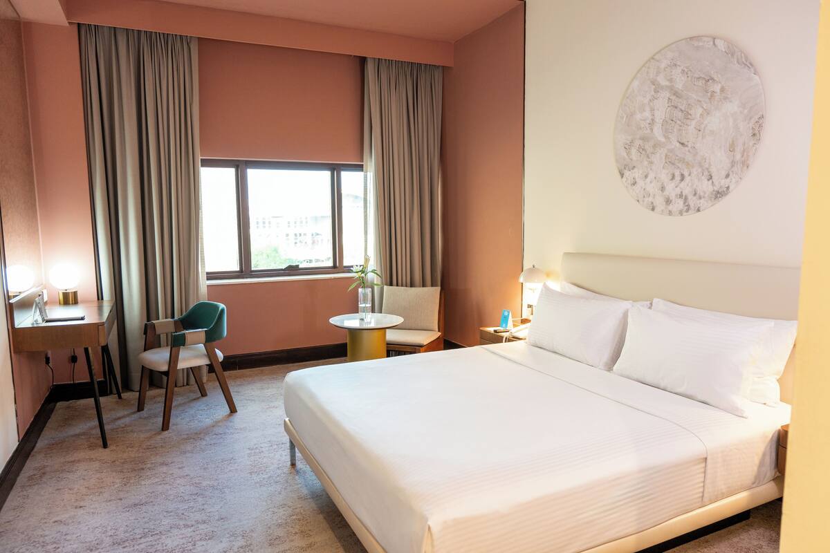 Een hotelkamer met een bed, een bureau, een stoel, een ronde tafel en een raam met gordijnen.