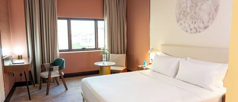 Ein Hotelzimmer mit Bett, Schreibtisch, Stuhl, rundem Tisch und einem Fenster mit Vorhängen.