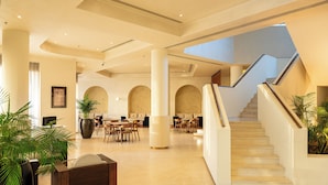 Un vestíbulo amplio con una escalera, zonas de estar y grandes columnas.