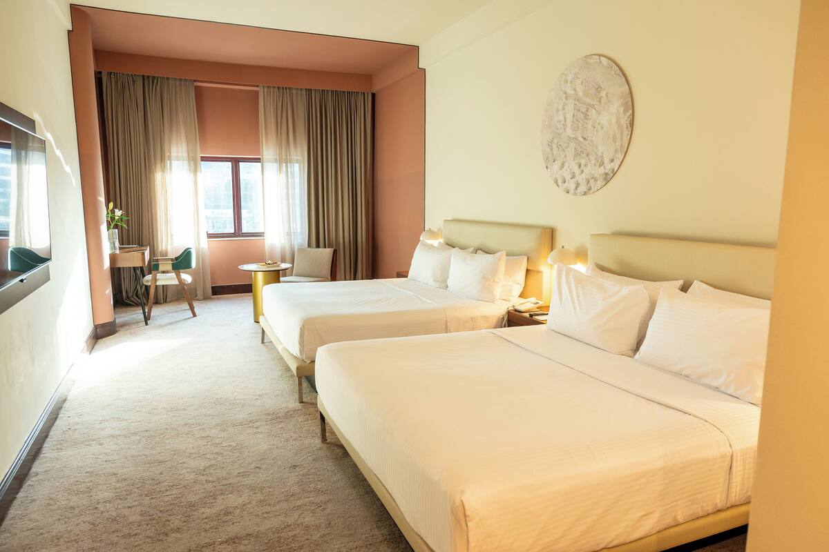 Een hotelkamer met twee bedden, een bureau, een stoel en een groot raam met gordijnen.
