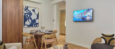 Een moderne woonkamer met een eethoek, een aan de muur bevestigde televisie, en een houten vloer.